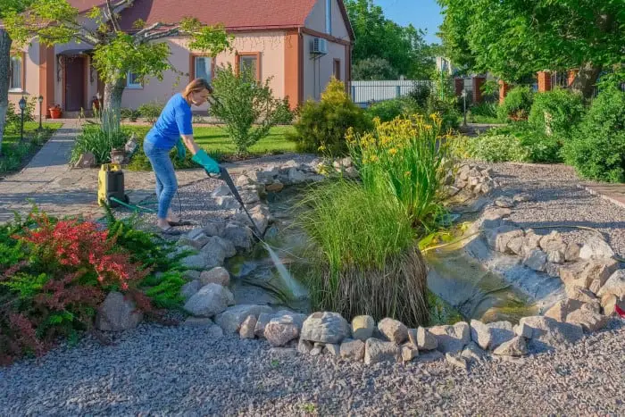 woman cleaning a backyard pond with a pressure washer
