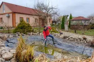 Man cleaning backyard garden pond with a net