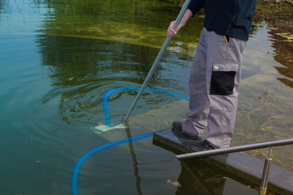 Person vacuuming the bottom of a dirty pond